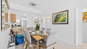A dining area with a wooden table, grey chairs, and a blue storage bin. - Poolside Bliss: 2-Bedroom Condo with Patio Noord (Noord)