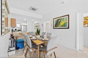 A dining area with a wooden table, grey chairs, and a blue storage bin. - Poolside Bliss: 2-Bedroom Condo with Patio Noord (Noord)