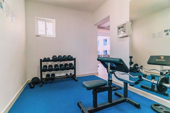 A gym with a bench press, dumbbells, and a weight rack.