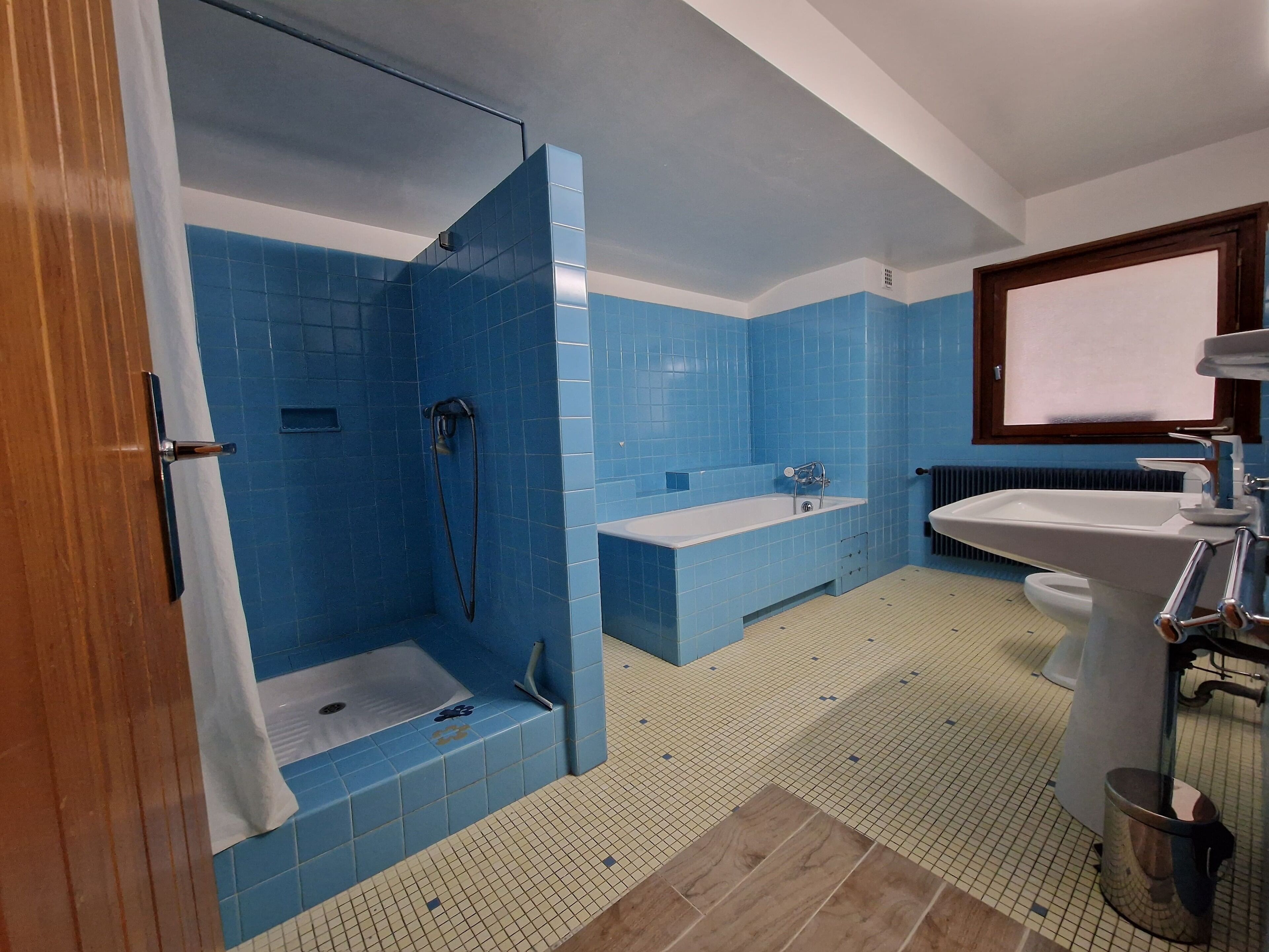A bathroom with blue tiles, a bathtub, a shower, a sink, and a toilet.