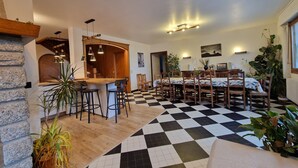 A dining area with a checkered floor, wooden furniture, and a bar area with stools. - Guy and Rose's cottage (Passy)