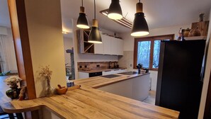 A modern kitchen with wooden countertops, black pendant lights, and a black refrigerator. - Guy and Rose's cottage (Passy)