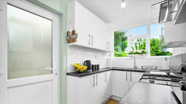 Una cocina moderna con armarios blancos, encimera negra y ventana con vistas a zonas verdes.