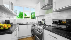 Cocina moderna con armarios blancos, estufa a gas, horno empotrado y lavavajillas. Una ventana ofrece vistas a la vegetación exterior.
