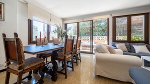 A dining area with wooden chairs and a table, a sofa, and a view of the outdoors through large windows. - El Ranchito, villa in Paguera, Majorca, quiet area, with swimming pool and barbecue. (Peguera)