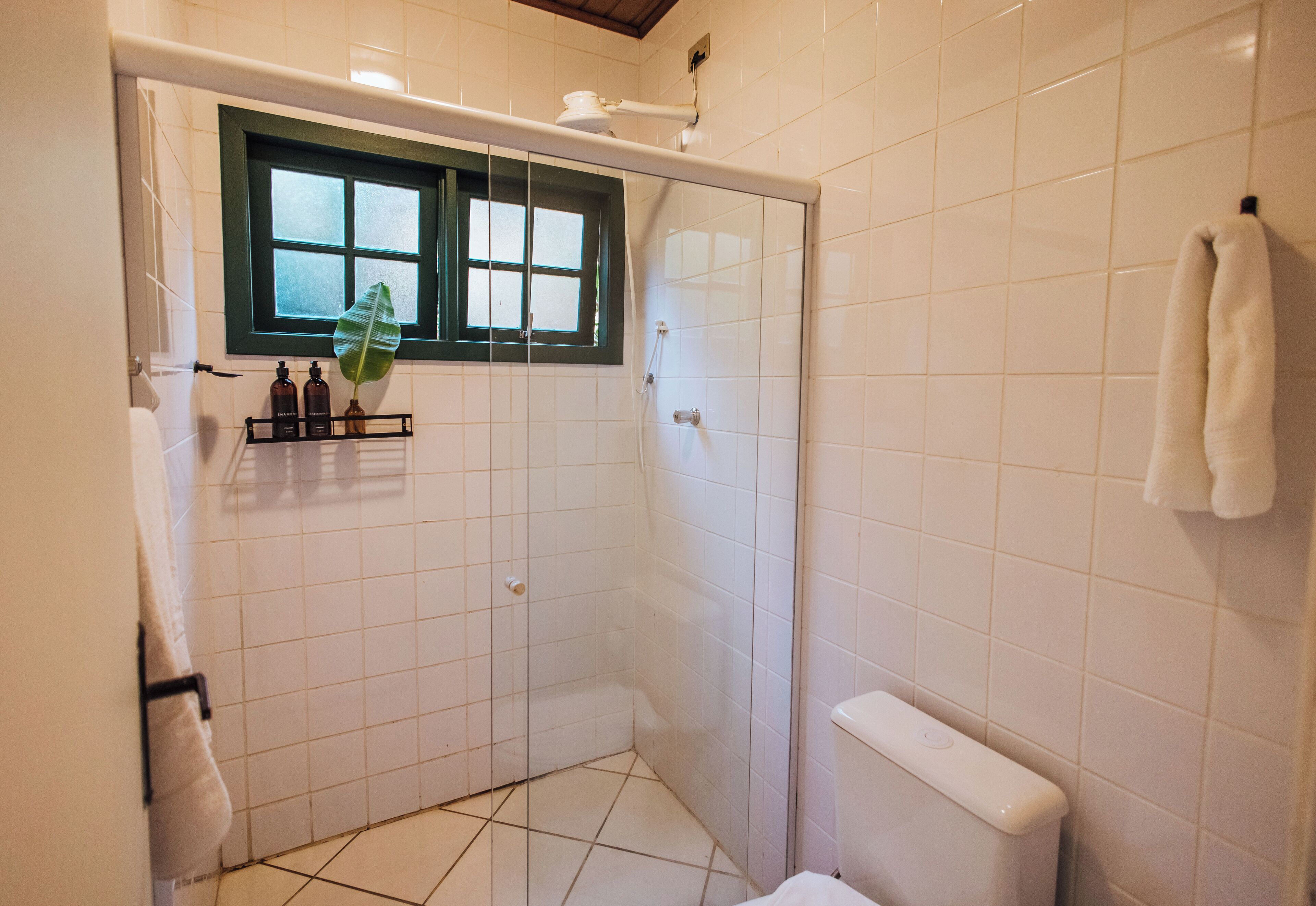 Une petite salle de bain carrelée, équipée d’une douche, de toilettes et d’une fenêtre.