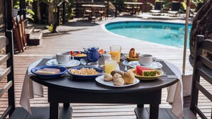 A dining table with breakfast items and a pool in the background. - Pousada Vila das Pedras (Ilhabela)