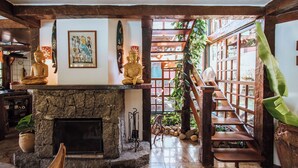 A traditional interior with a stone fireplace, wooden staircase, and two golden Buddha statues. - Pousada Vila das Pedras (Ilhabela)
