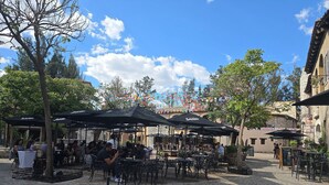 Un área de café al aire libre con mesas y sillas, rodeada de adoquines.