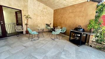 An outdoor patio with a table and chairs, a grill, and potted plants.