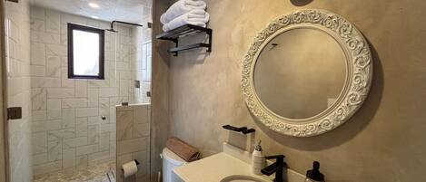 A bathroom with a marble-tiled shower, a toilet, a sink with a mirror, and a towel rack.