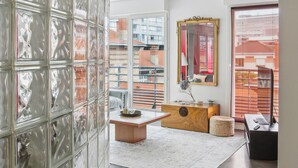 A modern living room with a glass partition, a wooden coffee table, a mirror, and a view of the cityscape through large windows.