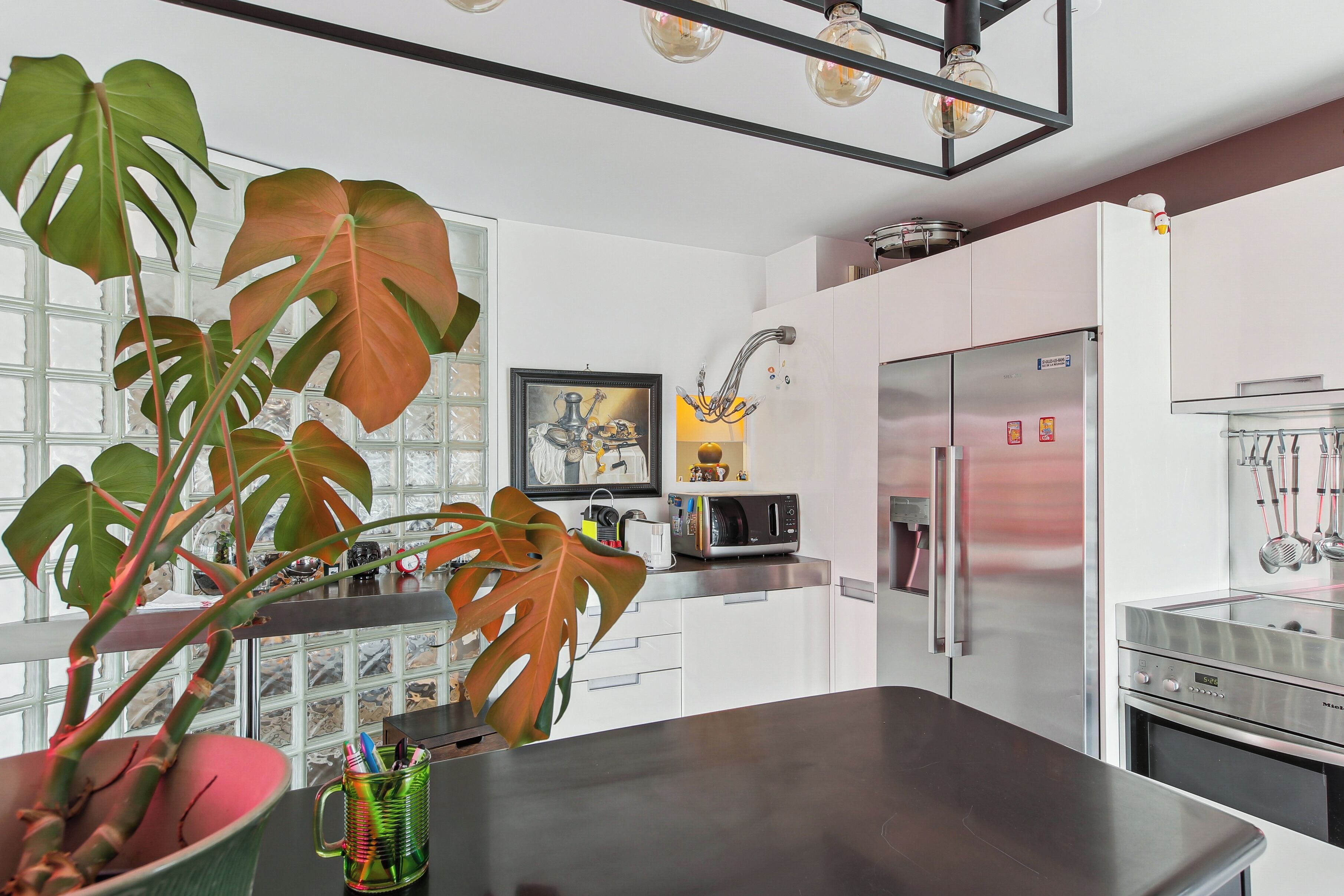 A modern kitchen with white cabinets, stainless steel appliances, and large windows.