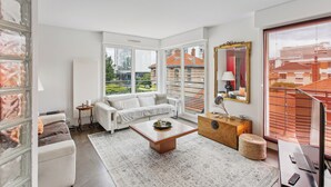 A modern living room with a white sofa, a coffee table, and a view of the city through large windows.