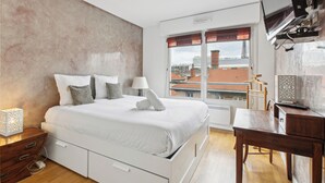 A bedroom with a large bed, bedside tables, a desk, and a TV mounted on the wall.