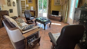 A living room with a sofa, armchairs, a coffee table, and a television. There is a door leading outside, and the room has patterned flooring. - Villa Torre Blanca in Farinole (Farinole)
