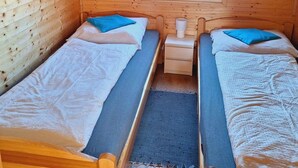 Mökki, jossa on kaksi puista sänkyä, pieni yöpöytä ja ikkuna.