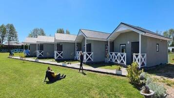 A row of single-story cabins with white railings, a grassy lawn, and a clear blue sky.