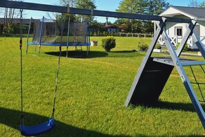 Un jardin avec un trampoline, une balançoire et un petit abri de jardin.