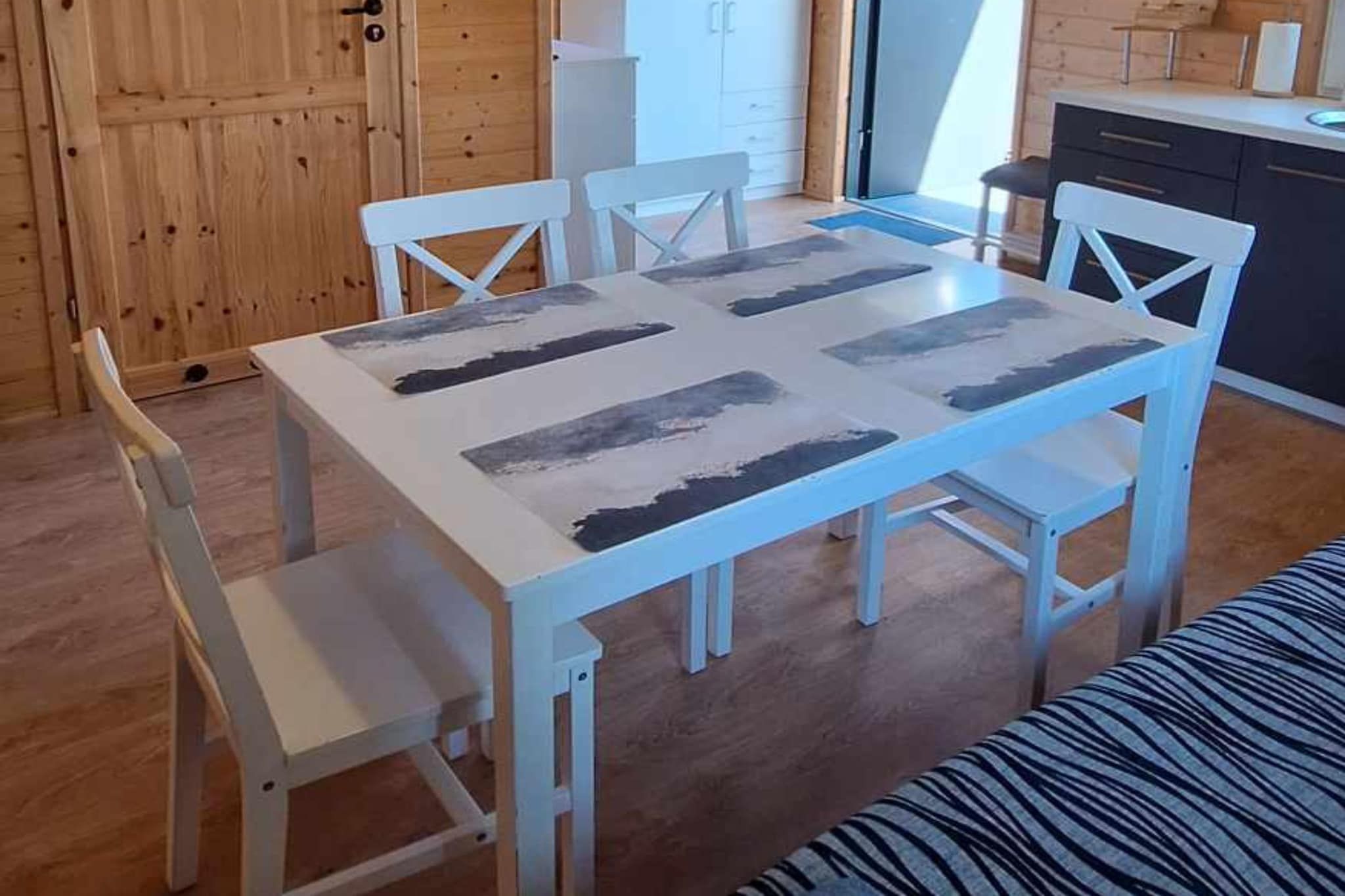 A dining area with a white table and chairs, a bench, and a kitchen in the background.
