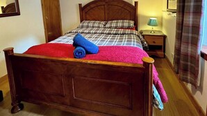 Una cama bien hecha con cabecera de madera, una lámpara de noche y un cuadro enmarcado encima.