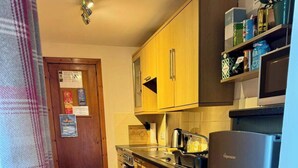 Una cocina compacta con armarios de madera, lavadora de acero inoxidable, refrigerador y una pequeña encimera con hervidor y cafetera.