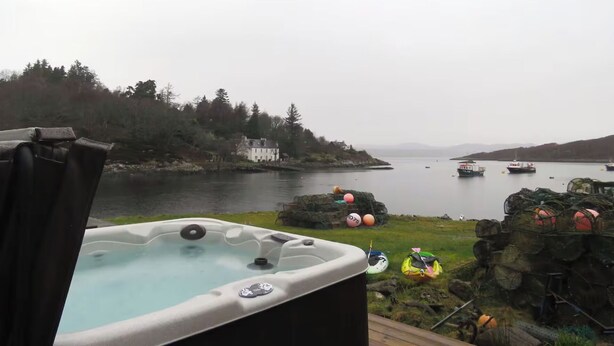 Un jacuzzi en una terraza con vistas a un lago con barcos y una casa al fondo.