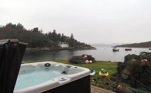 Un jacuzzi en una terraza con vistas a un lago con barcos y una casa al fondo.
