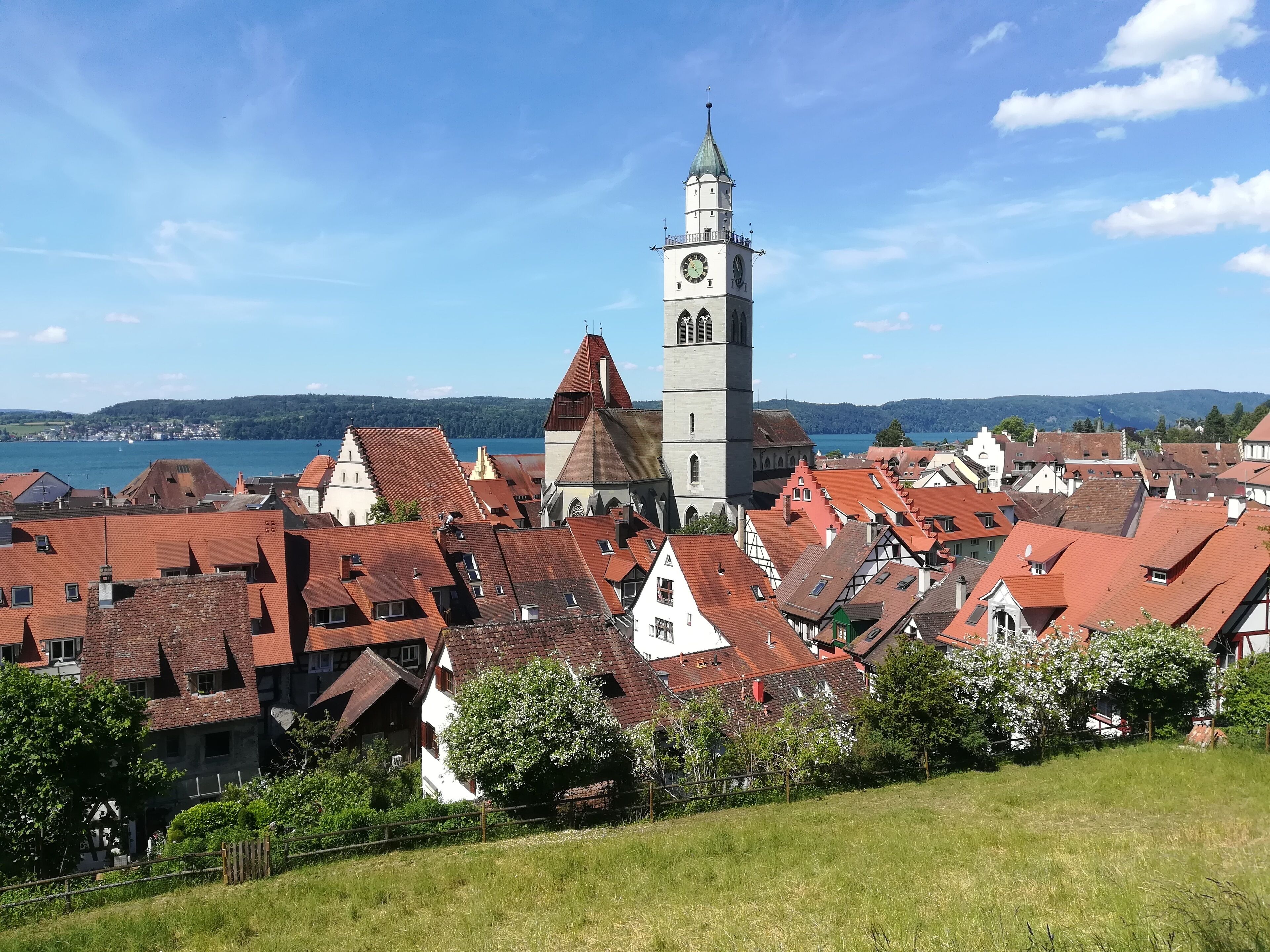 Eine historische Stadt mit traditioneller Architektur, einem markanten Glockenturm und einem See im Hintergrund.