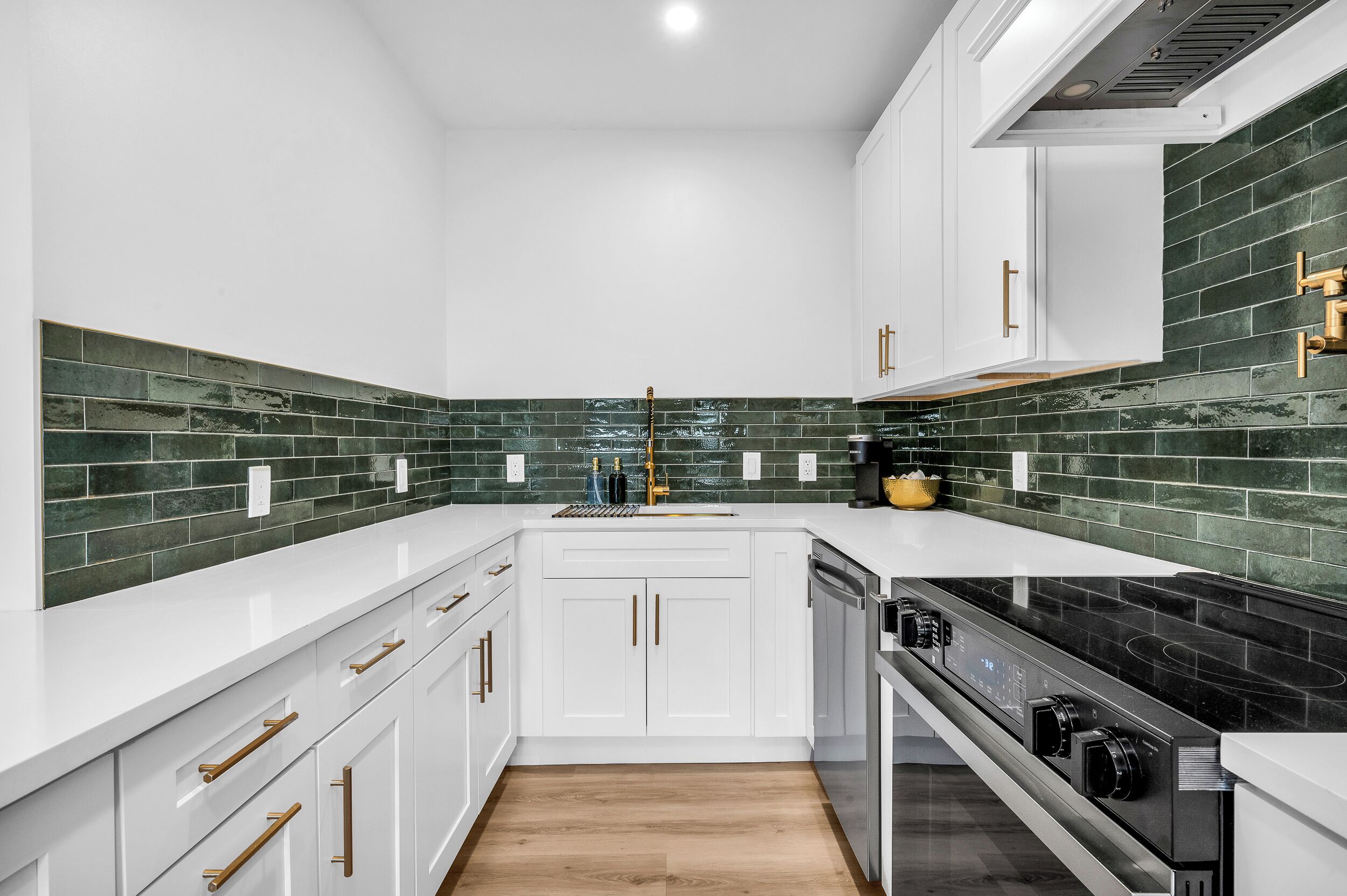 A modern kitchen with white cabinetry, a black stove, and green-tiled backsplash.