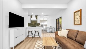 Una cocina moderna con armarios blancos, un televisor de pantalla plana grande y una zona de comedor con taburetes.