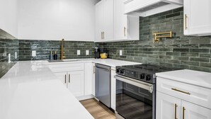 Una cocina moderna con armarios blancos, estufa negra y salpicadero de azulejos verdes.