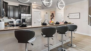 A modern kitchen with dark cabinets, a stainless steel refrigerator, and a central island with bar stools. - Immersive Activities, Arcade, Theatre Sleeps 24 (Davenport)