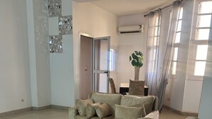 Sala de estar com um sofá seccional bege, um tapete felpudo branco e um vaso com planta.