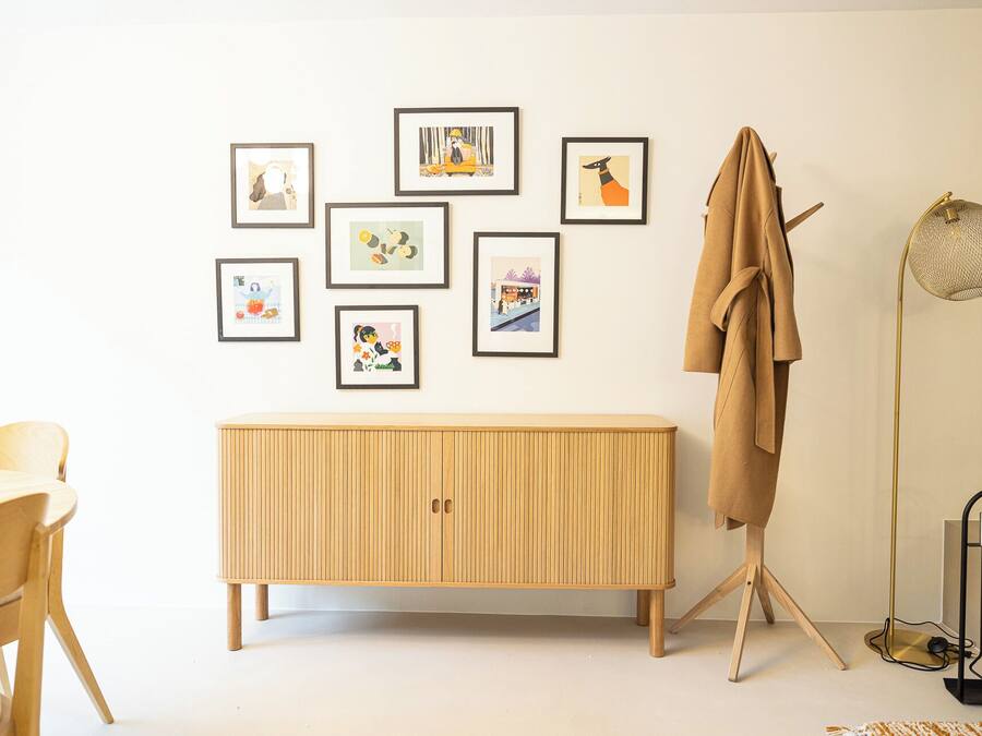 A room with a wooden cabinet, a coat rack, a floor lamp, and several framed pictures on the wall.