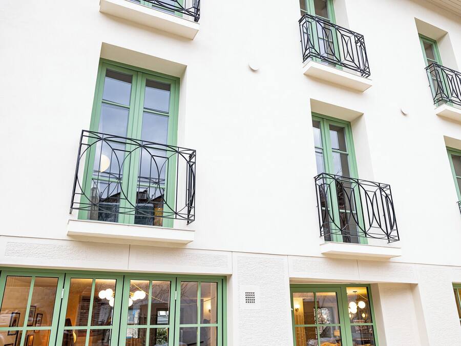 A multi-story building with green-framed windows and black metal balconies.