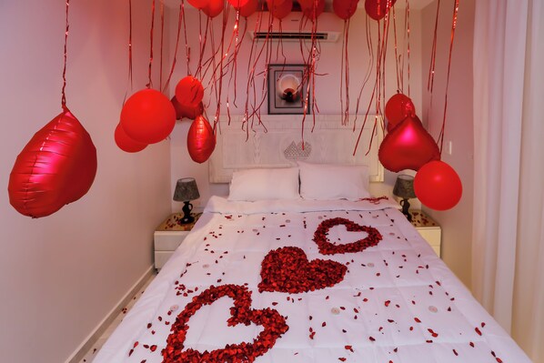 A bed with rose petals arranged in heart shapes, red balloons, and a white bedspread. - Pyramids Land View (Giza)