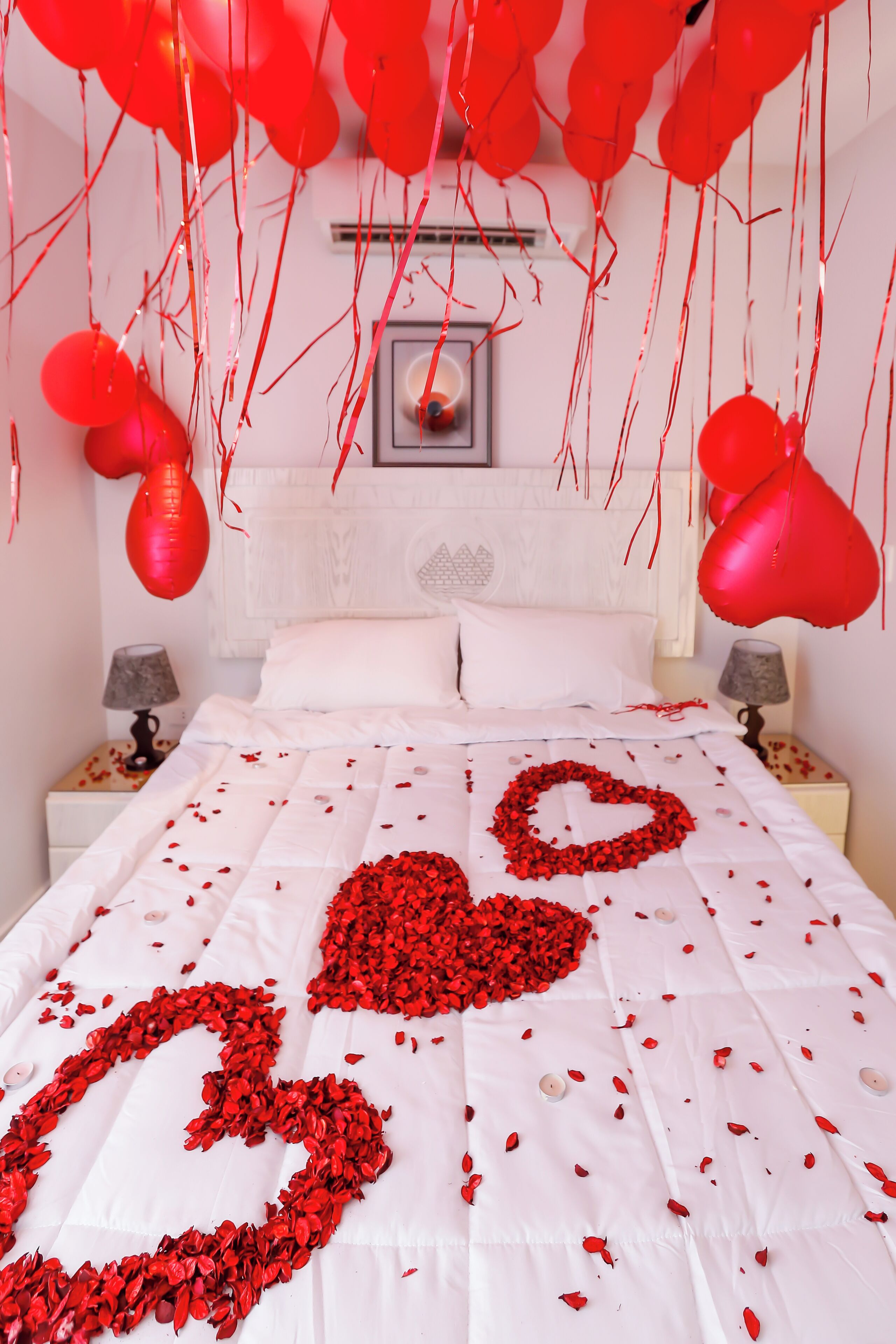 Una cama con un arreglo de pétalos de rosa y globos rojos en forma de corazón.