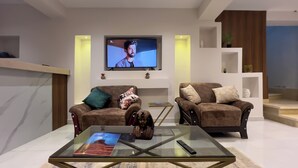 Un salon moderne avec deux canapés, une table basse en verre et un téléviseur fixé au mur.