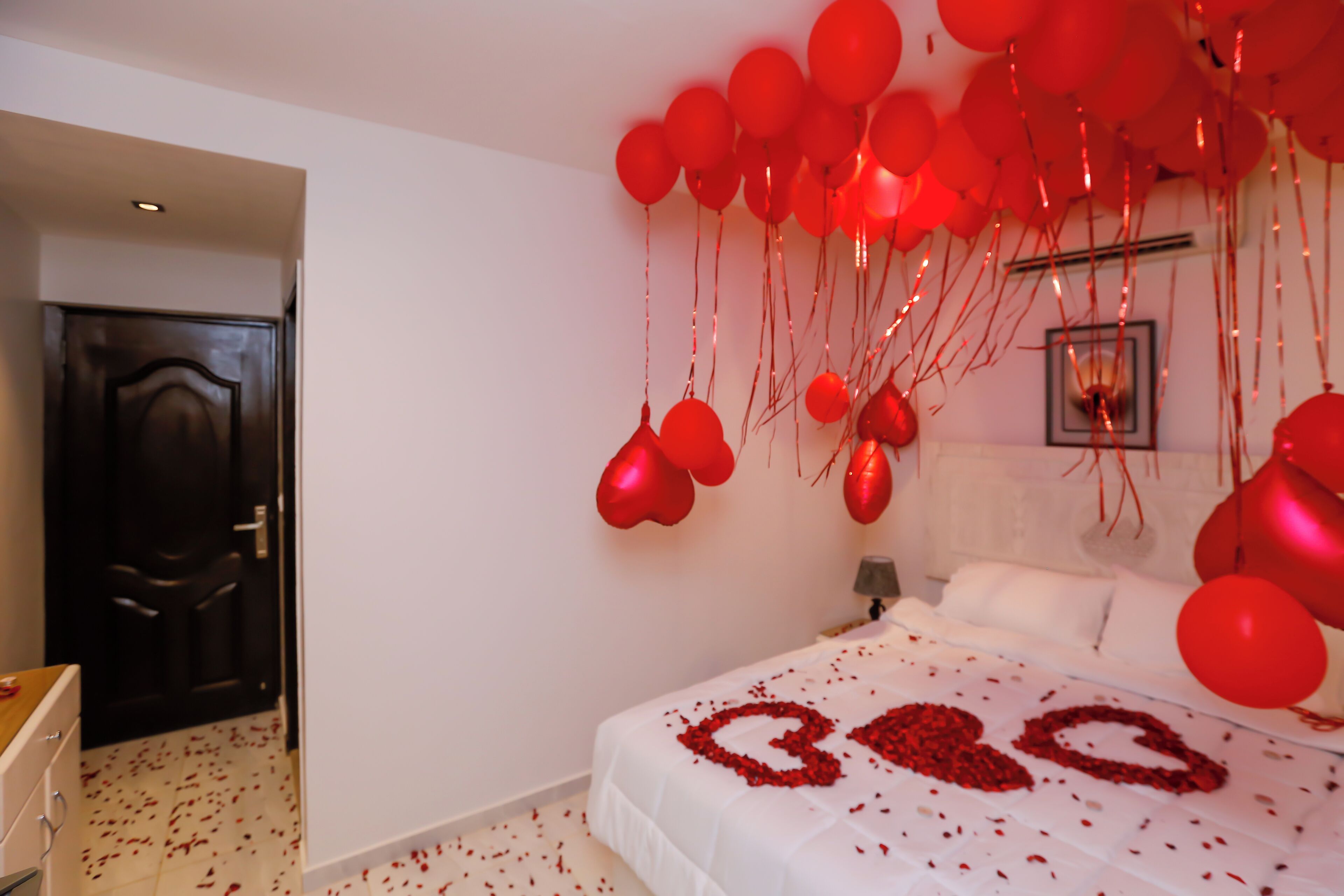 A bedroom with a bed, a door, and red balloons.