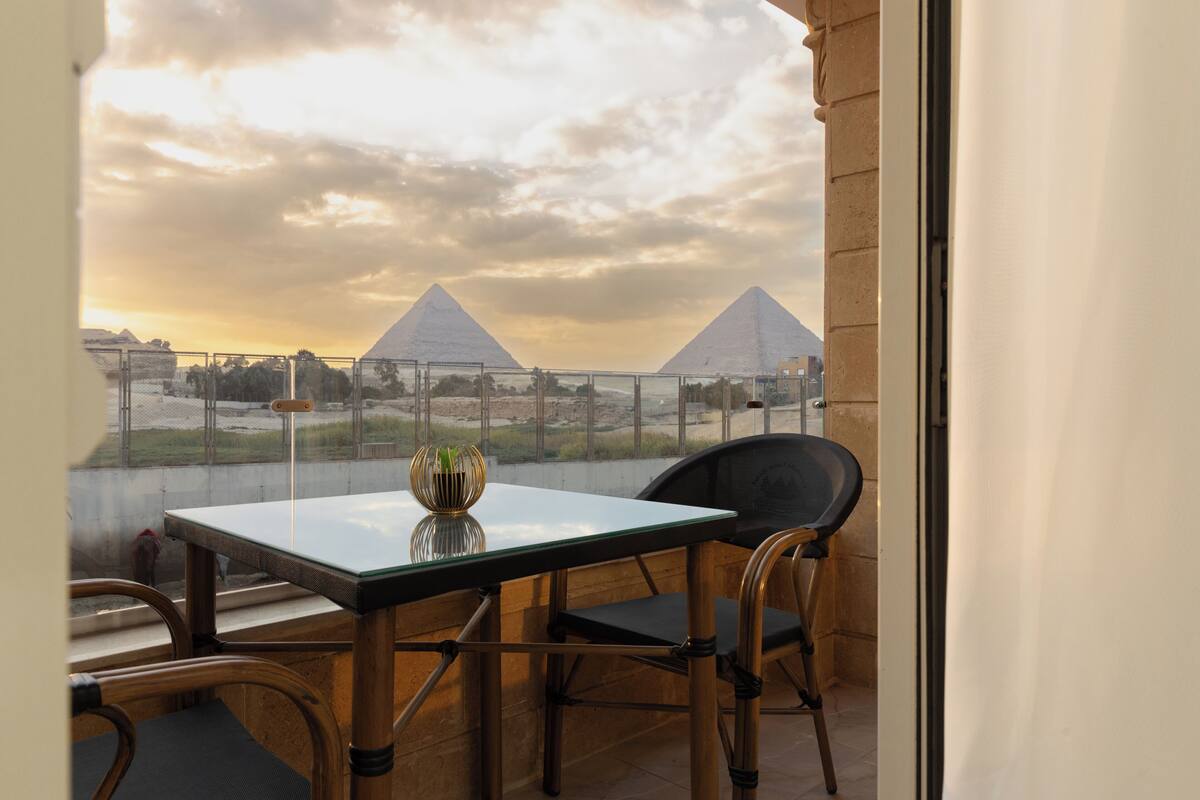 En balkon med et bord og stole, med udsigt over pyramiderne.