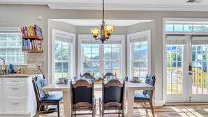 A dining area with a large table, four chairs, and a chandelier. There are bookshelves and a window with a view of a playground. - Heated Pool King Bed Jacuzzi Bath Arcade (Winston-Salem)