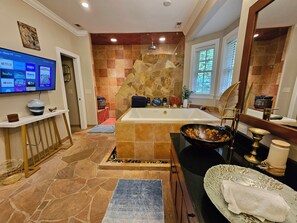 A modern bathroom with a stone wall, a large bathtub, and a vanity with a gold faucet. - Heated Pool King Bed Jacuzzi Bath Arcade (Winston-Salem)