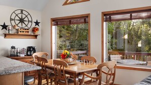 A dining area with a wooden table and chairs, a kitchen counter, and large windows with a view of trees. - Wilderness Ridge | Private Cabin w/ Mountain Views (Linden)