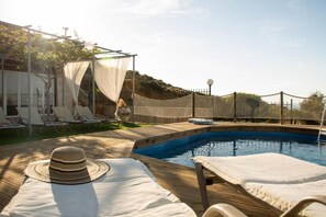 Relax by the pool surrounded by a fence, with lounge chairs and a shaded seating area.
