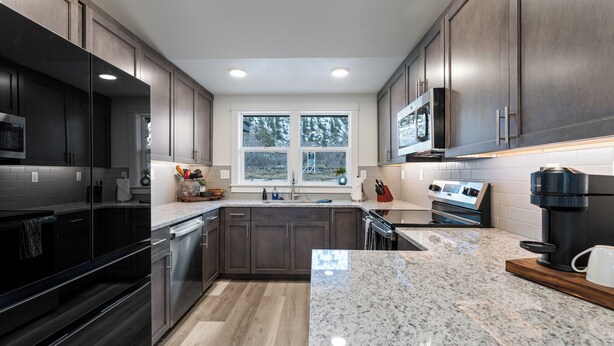 Cocina moderna con alacenas de madera oscura, encimeras de granito, electrodomésticos de acero inoxidable y un ventanal con vistas a árboles.
