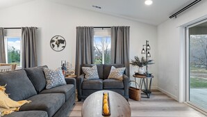 Una sala de estar moderna con un sofá gris, un sillón a juego, una mesa de centro de madera y un ventanal con cortinas.