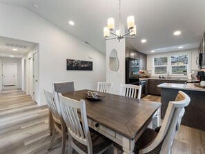A modern kitchen with a central island, white cabinetry, and a dining area with a wooden table and chairs.