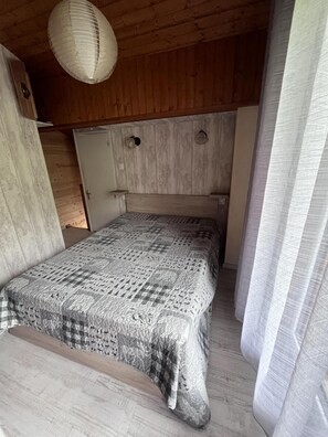 A bedroom with a wooden ceiling, a bed with a patterned bedspread, and a hanging light fixture.