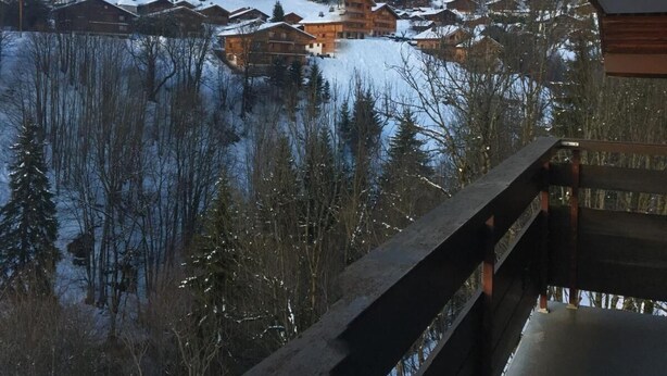 En fjällstuga med en träfasad, omgiven av snötäckta träd och med en vacker utsikt över en sjö.